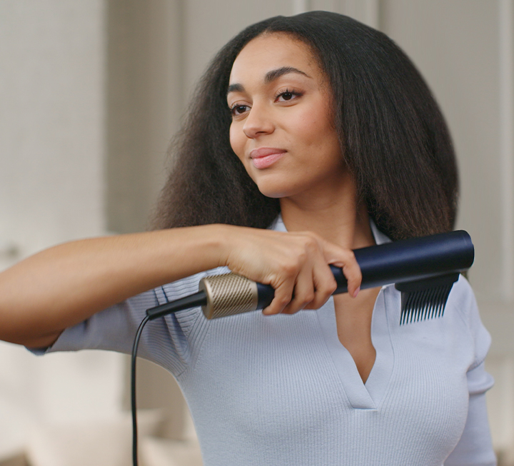 Mujer estirando y desenredando el cabello natural con el tubo secador InfinitiPRO de Conair DigitalAire